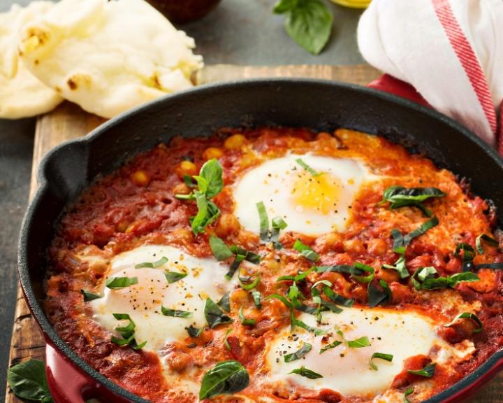 Shakshuka in a skillet: three eggs poached in tomato sauce with chickpeas and greens.