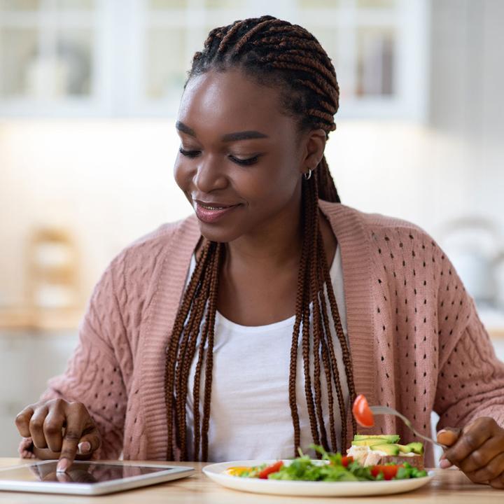 African American woman eating salad and looking at tablet computer