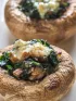 Two stuffed mushrooms with spinach and melted cheese on a white plate.