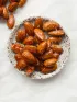 Glazed almonds in a small bowl, with more scattered on white.