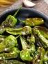 Blistered green peppers with sea salt in a black pan