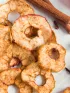 Dried apple slices, whole red apples, cinnamon sticks, and spices on a white surface.