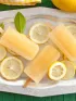 Four refreshing lemon popsicles on a silver tray with lemon slices and leaves.