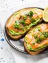 Two slices of toast topped with mashed avocado, smoked salmon, and herbs