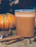 pumpkin almond smoothie in a glass with cinnamon sticks and pumpkins in the background