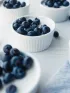 Small white bowls of yogurt mousse topped with fresh blueberries on a light surface.