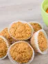 Muffins in white liners next to a green bowl of baby carrots.