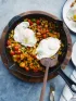 Skillet with colorful vegetable hash, two fried eggs. Two servings ready on plates.