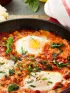Shakshuka in a skillet: three eggs poached in tomato sauce with chickpeas and greens.