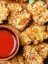 Crispy chicken nuggets with nutty crust and a small bowl of red dipping sauce.