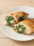 Two baked chicken breasts, sliced to show a green spinach filling, on a white plate.