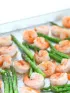 Cooked shrimp and asparagus spears on a metal baking sheet.