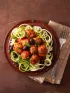 Plate with zucchini spaghetti, meatballs, tomato sauce, and black olives.