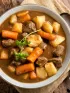 Bowl of hearty beef stew with meat, carrots, potatoes, and parsley garnish.