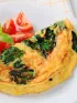 Tomato and basil omelet with tomato wedges and basil on a white plate.