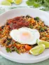 A bowl with cauliflower rice, peppers and black beans topped with a fried egg. Served with lime wedges. 