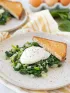 Two plates with sautéed spinach, onions, poached eggs, and toast. Eggs in background.