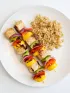 Two grilled tofu and colorful vegetable skewers with brown rice.
