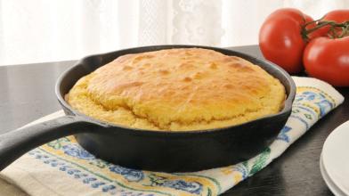 Cornbread in an iron cast skillet with tomatoes on top of a towel.