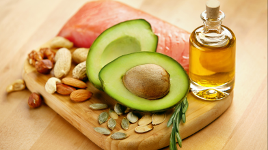 A wooden board with healthy fats like avocado, olive oil, and nuts for a healthy diet.