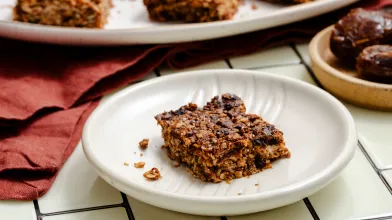 A plate with a slice of California date breakfast bar with more bars in the background for healthy sweet snack