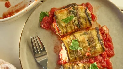Eggplant rolls served on a plate with tomato sauce.