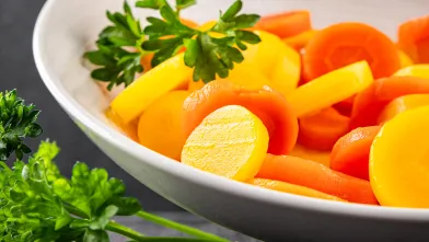 steamed yellow and organge carrot slices in bowl with parsely