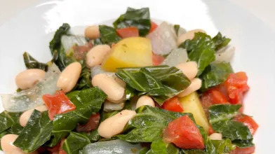 A plate of cooked collard greens, white beans, and potatoes. 
