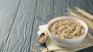 Bowl of oatmeal, scattered oats, wooden scoop, and wheat on a rustic grey table.
