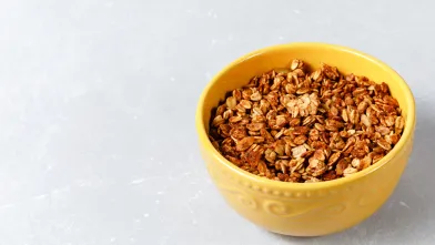Yellow bowl filled with gluten-free granola on a light gray surface.