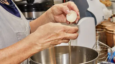 Woman cracking an egg to get egg white into stainless steel bowl for cooking