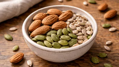 Bowl with almonds, green pumpkin seeds, and sunflower seeds on wood.