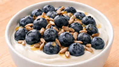 Bowl of yogurt topped with fresh blueberries, sunflower seeds, and a drizzle of honey.