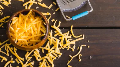 shredded low-fat cheddar cheese on wooden table next to grater