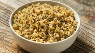 Bowl of cooked multi-colored quinoa on a wooden table.