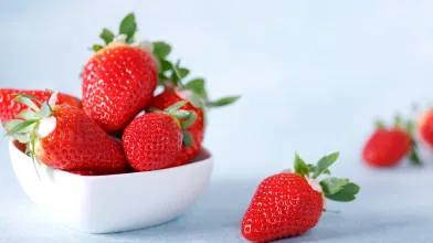 Bowl of fresh red strawberries on a light blue surface.