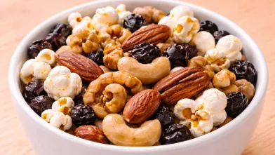 Small white bowl with a mix of popcorn, mixed nuts, and raisins
