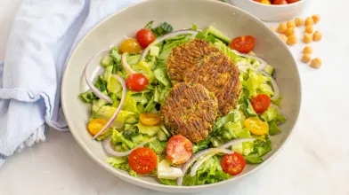 salad with three falafel patties, lettuce, cherry tomatoes, cucumber, and red onion in a bowl.