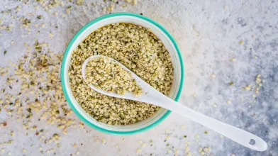 Bowl of hemp seeds with a white spoon on a light gray surface.