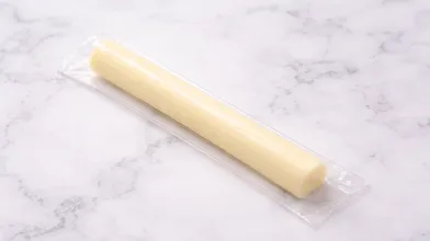 Single low-fat mozzarella cheese stick in plastic wrapping on countertop