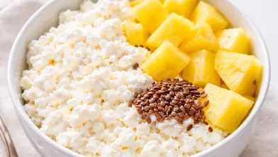 White bowl with cottage cheese, flax seeds, and pineapple chuncks