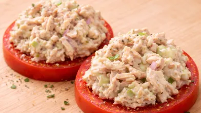 Healthy tuna salad on two tomato slices, sprinkled with herbs.