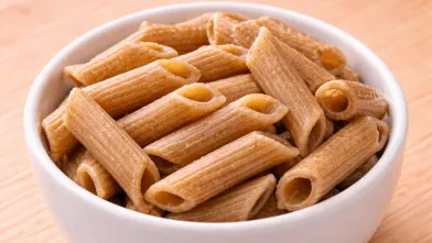 1/2 cup of whole grain penne pasta in small white bowl on brown cutting board