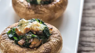Two stuffed mushrooms with spinach and melted cheese on a white plate.
