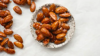 Glazed almonds in a small bowl, with more scattered on white.