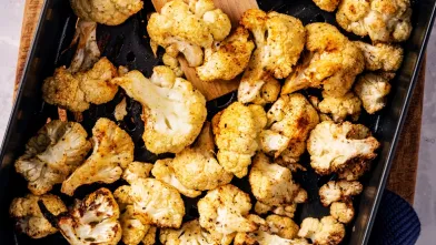 Golden-brown roasted cauliflower in a baking pan, with a wooden spatula.