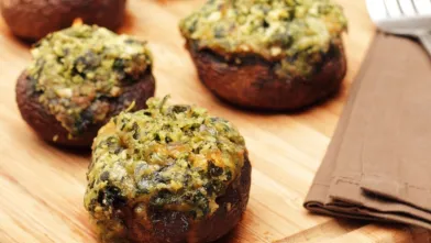 Five stuffed mushrooms with spinach and feta on a wooden board, a fork nearby.