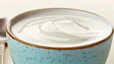 White yogurt in a speckled blue bowl with a spoon.
