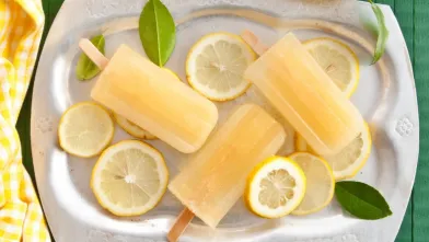 Four refreshing lemon popsicles on a silver tray with lemon slices and leaves.