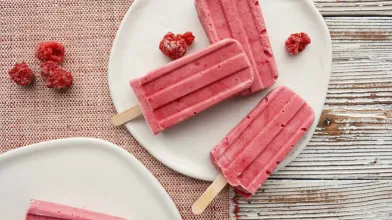 pink raspberry popsicles on white plates with scattered berries.